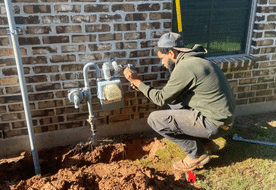 Technician working on a gas line next to a brick home