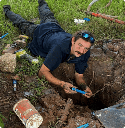 Plumber fixing an underground pipe in a dug-out yard